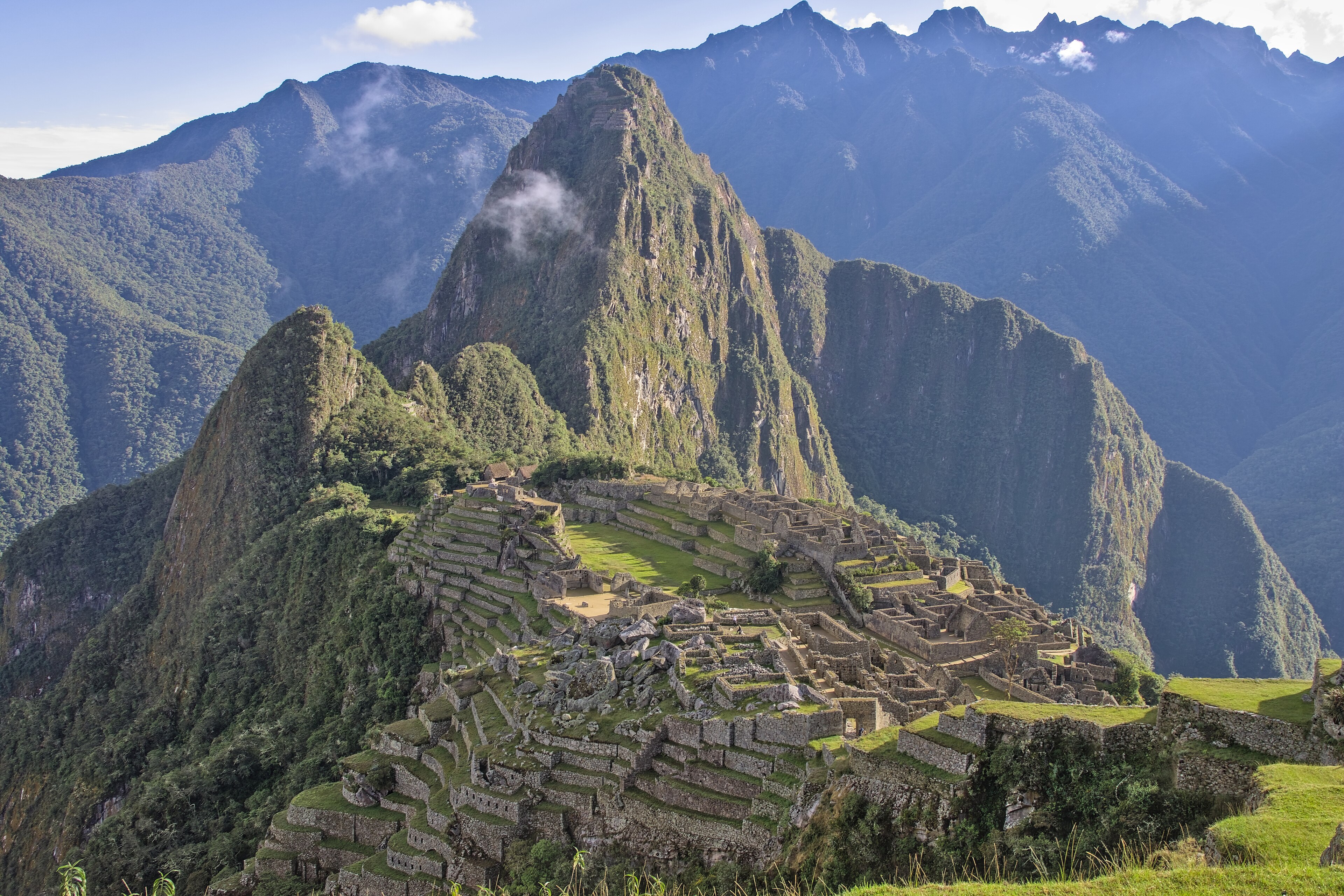 Veduta classica dall’alto di Machu Picchu: le rovine e le terrazze verdi ai piedi del monte Huayna Picchu, sotto un cielo azzurro.