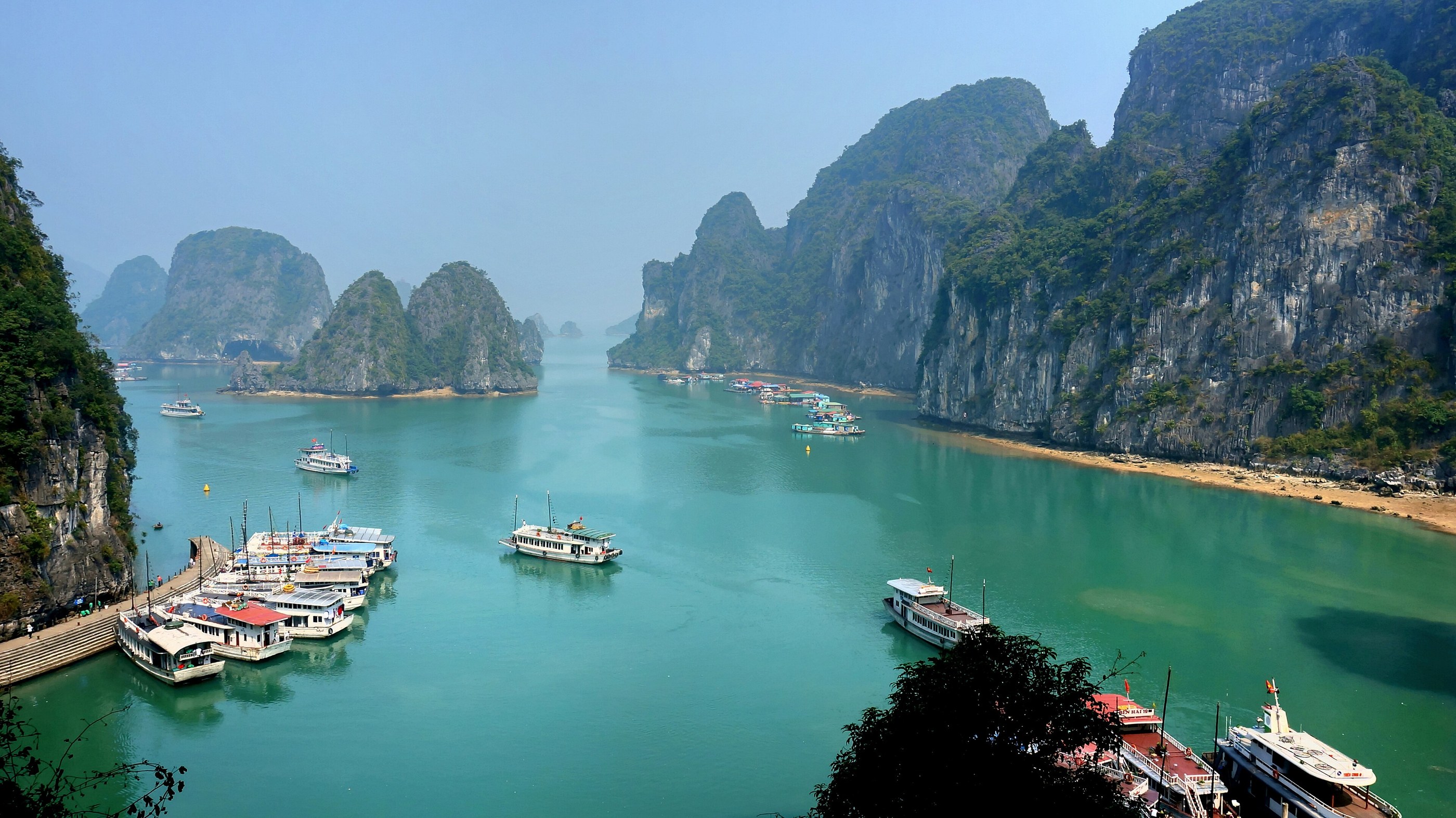 Barche nella baia di Ha Long, tra acqua turchese e alte scogliere verdi illuminate dal sole.