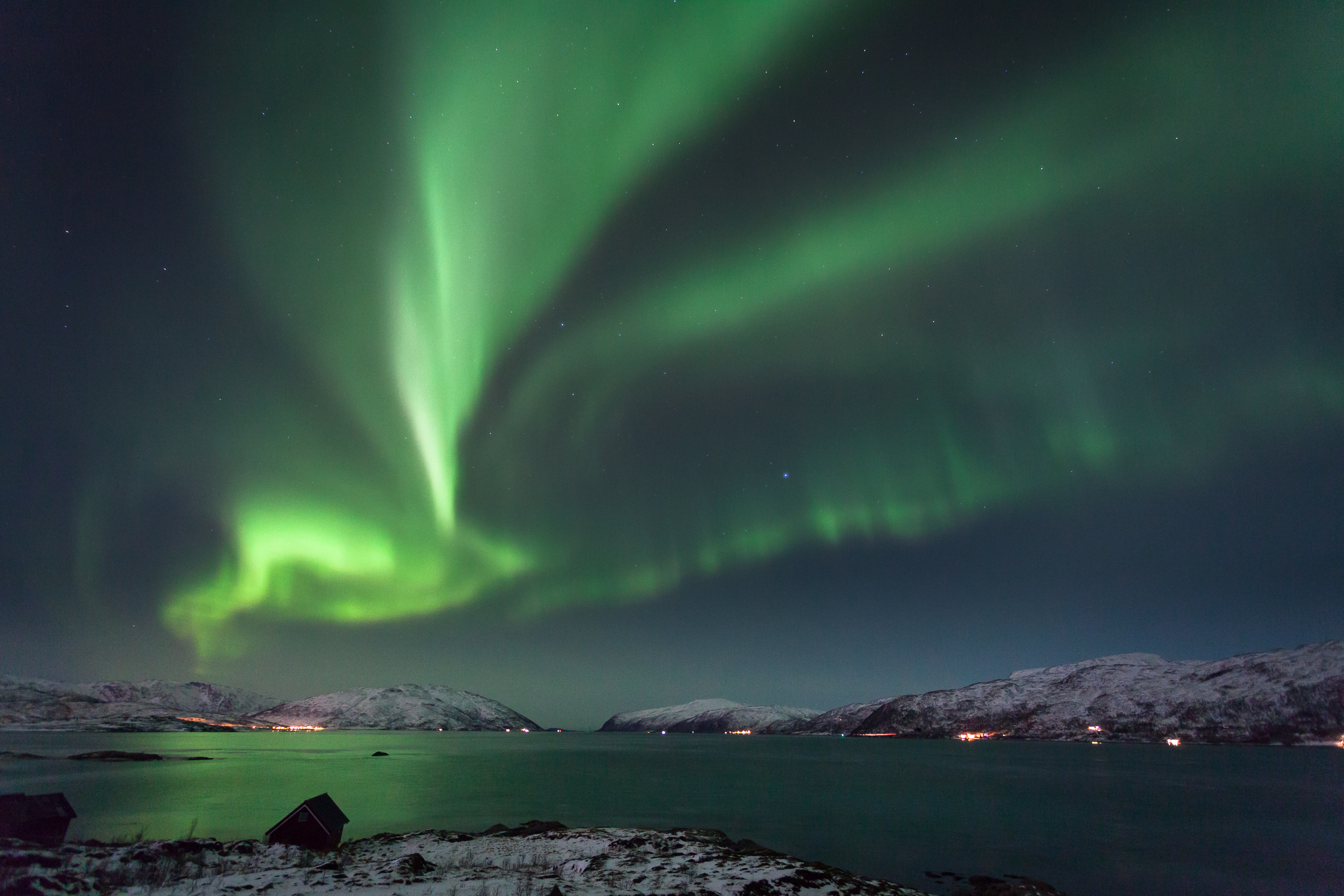 Aurora boreale verde sopra il fiordo e le montagne innevate di Kvaløya, a Tromsø