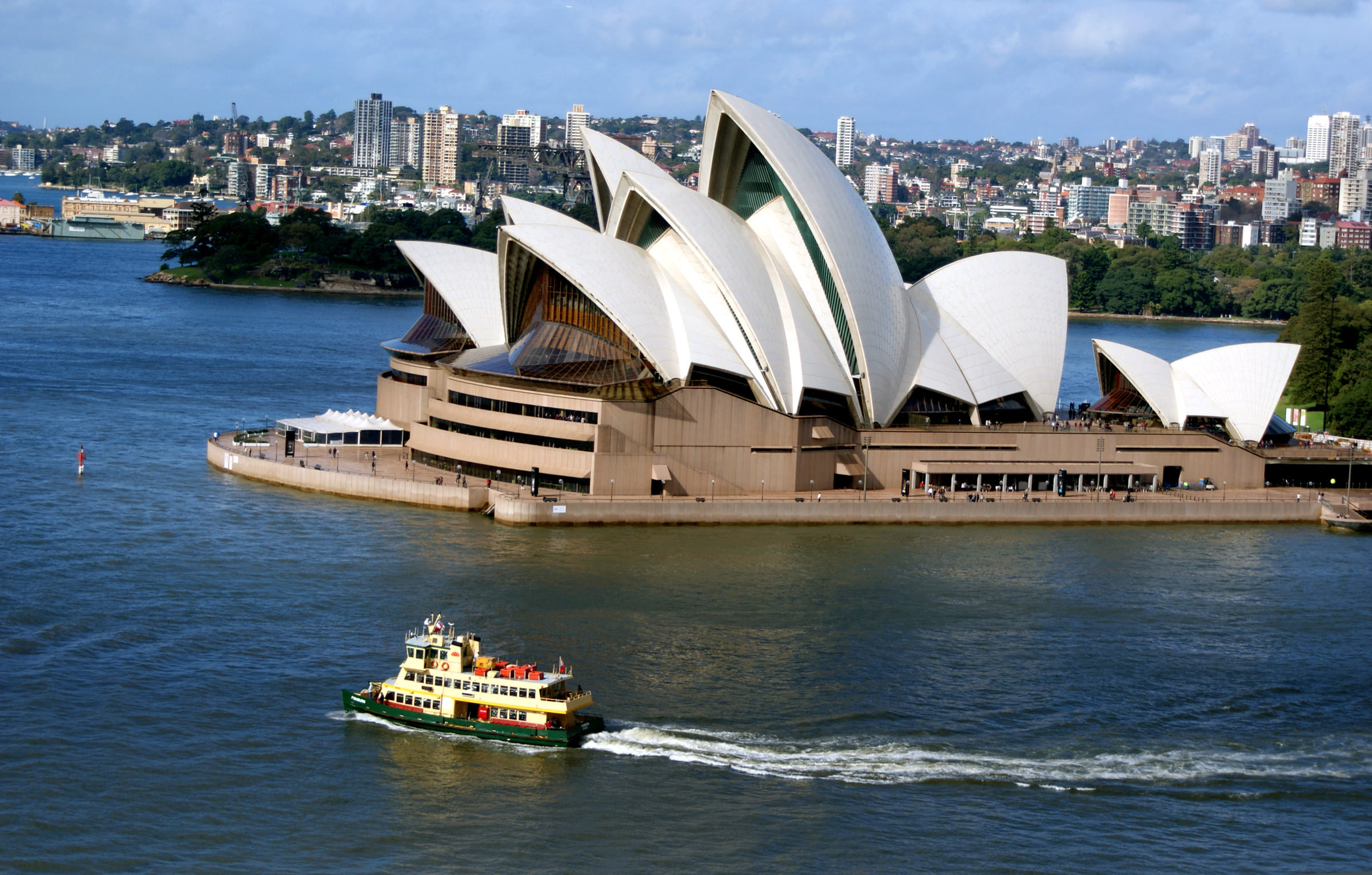 L’Opera House di Sydney affacciata sulla baia, con un traghetto colorato sul mare blu