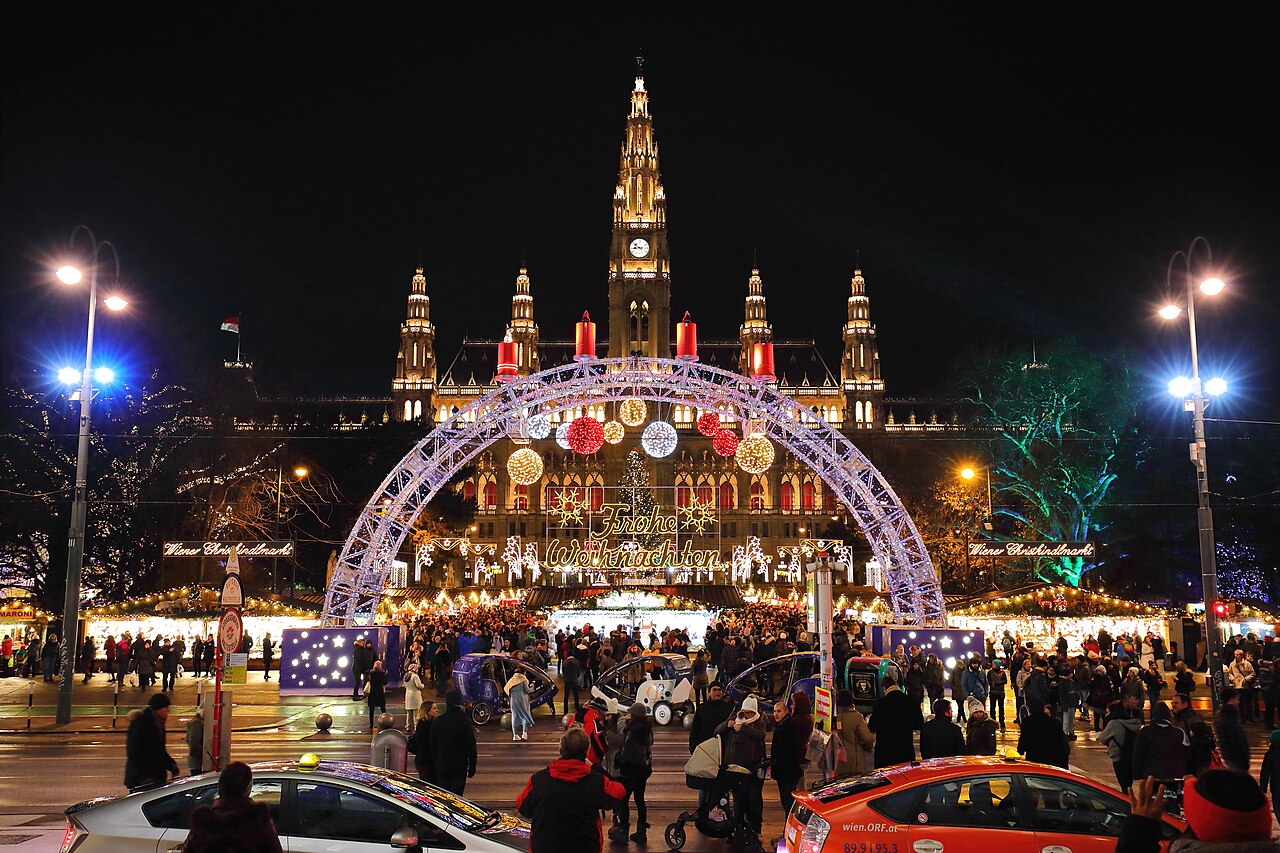 Il Rathaus di Vienna illuminato di notte dietro le decorazioni e il mercatino natalizio di Rathausplatz.