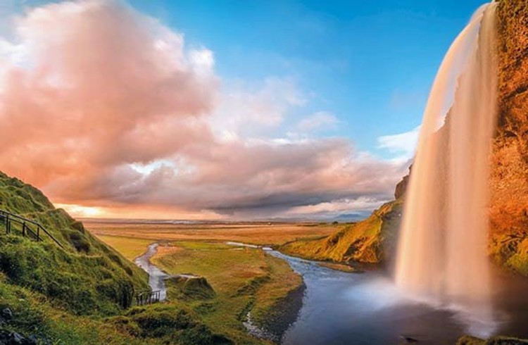 Isländischer Wasserfall zwischen grünen Wiesen und Sonnenuntergang