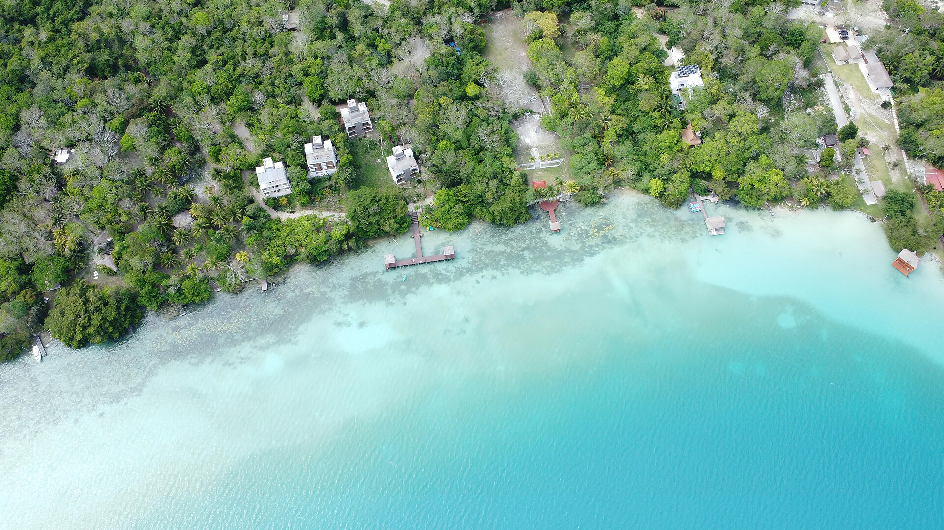 Veduta aerea della laguna di Bacalar, con acqua turchese, pontili e vegetazione lungo la riva.