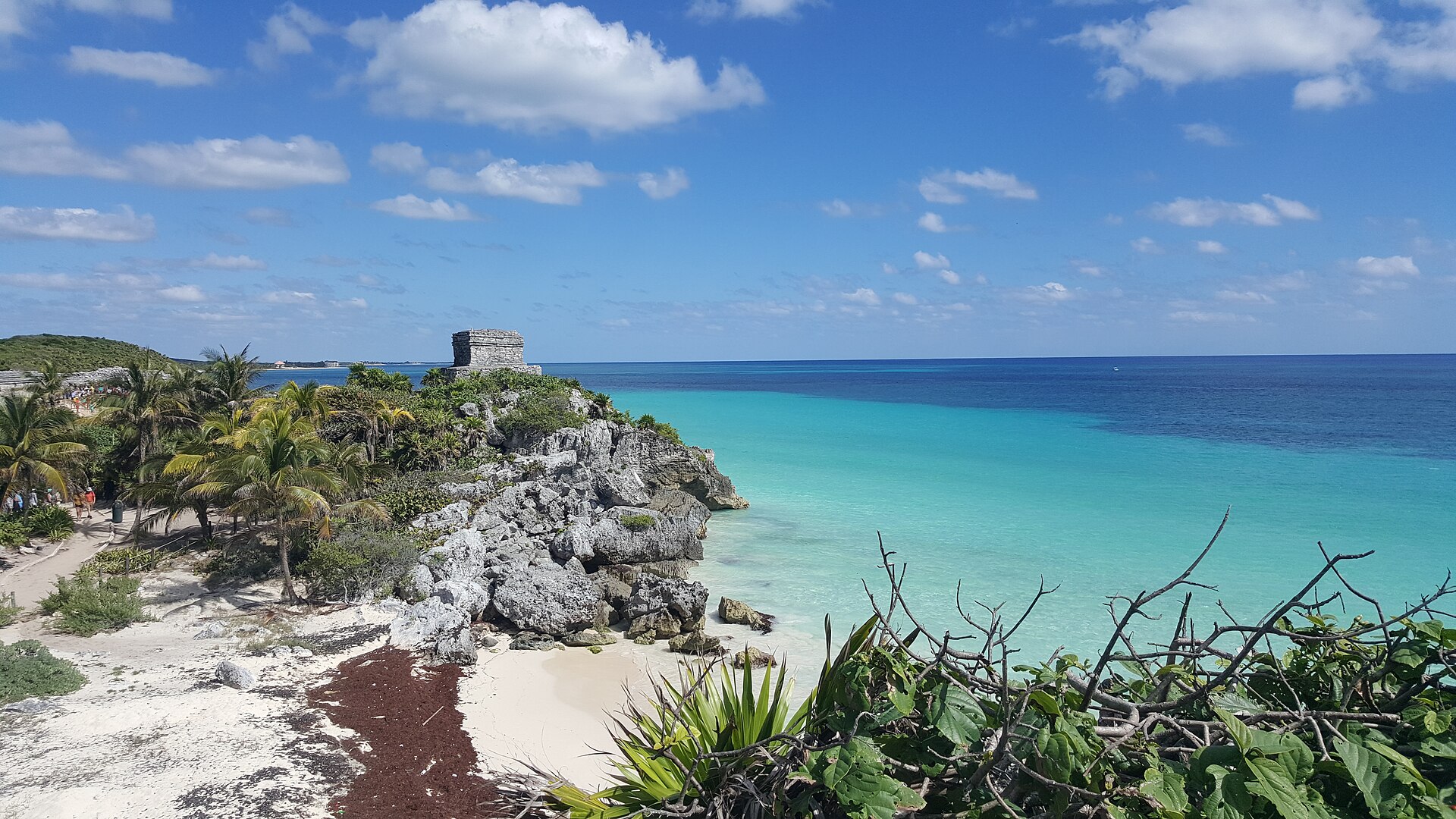 Rovine maya sulla scogliera di Tulum, tra palme, spiaggia chiara e mare turchese.